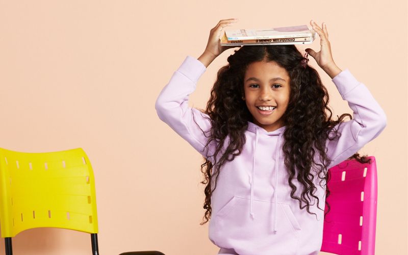 menina segura os livros sobre a cabeça e se prepara para a volta às aulas.