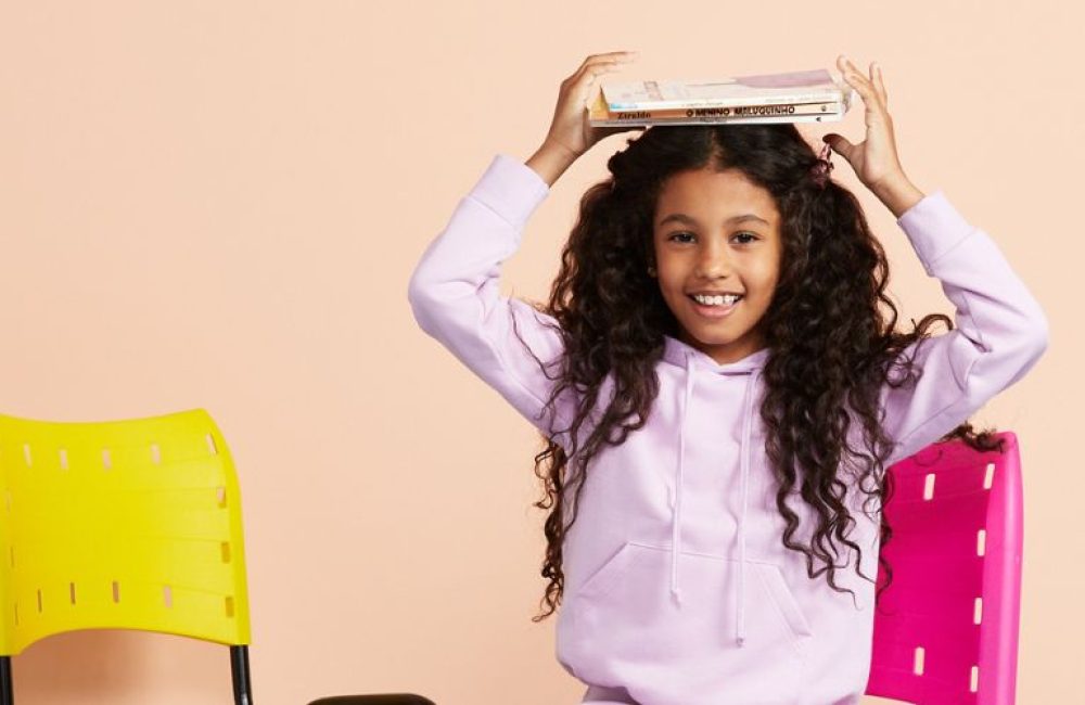 menina segura os livros sobre a cabeça e se prepara para a volta às aulas.